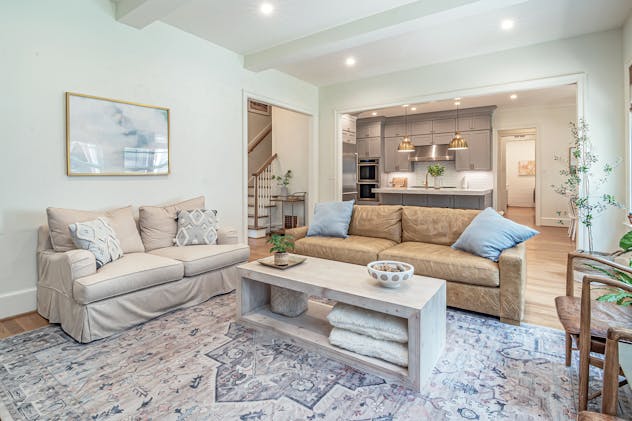 a white living room with beige couches and a grey kitchen in the background